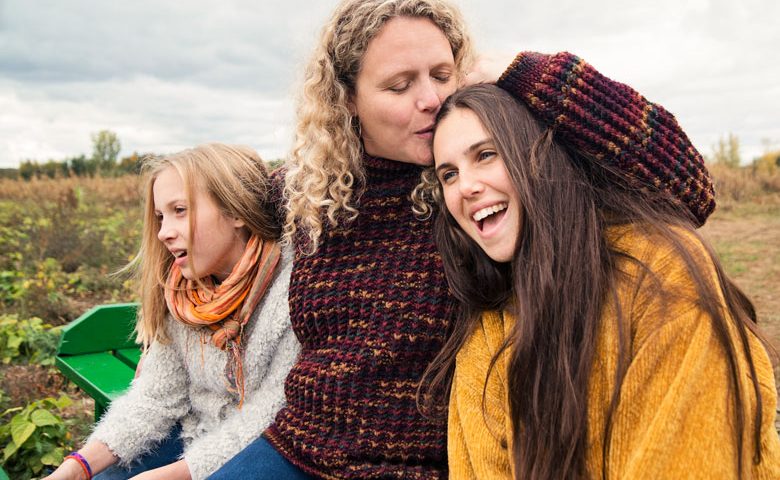 Mamma håller om sina döttrar och pussar ena på pannan